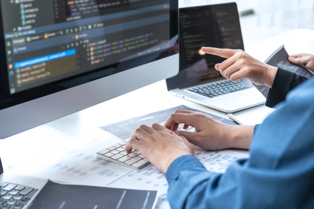 LiveWatch and AMS service showing developer monitoring code on multiple screens, representing real-time system supervision and application management services.