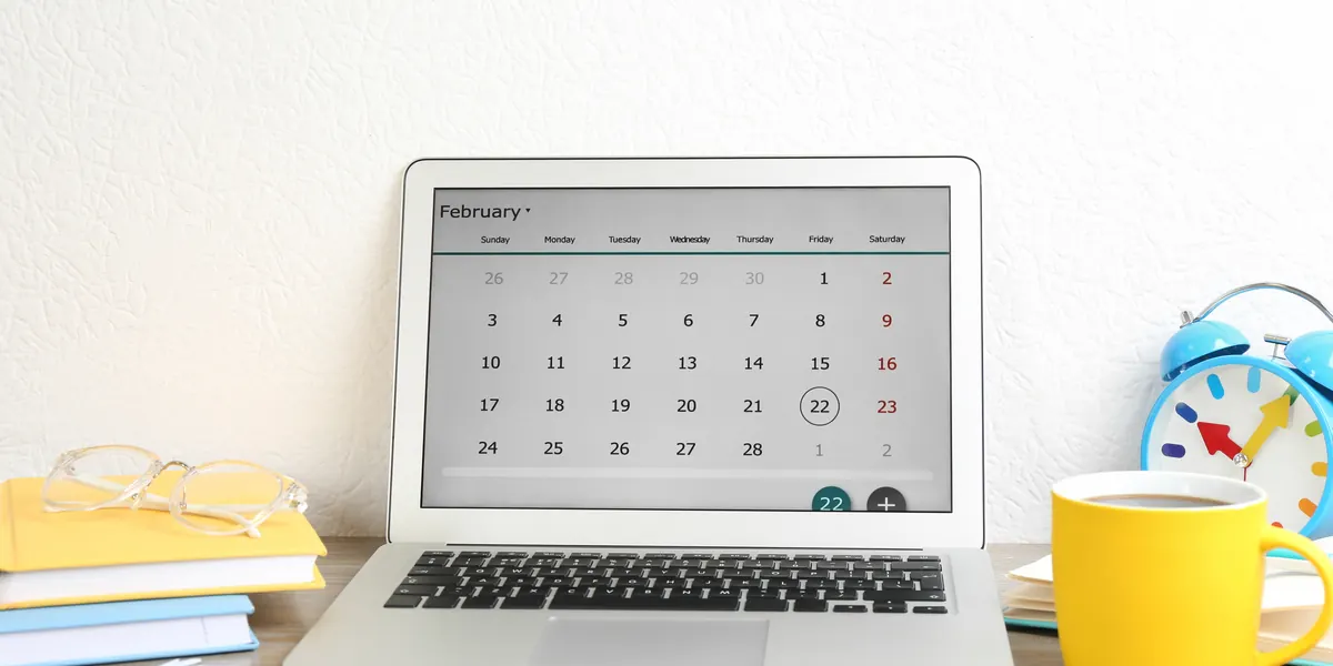 Portátil en el que se ve un calendario con una taza de café y un despertador