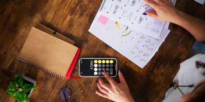 Professional reviewing financial reports and using a calculator on a smartphone for digital tax reporting and compliance analysis.