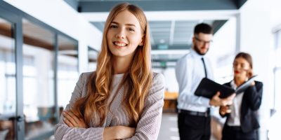 Stock image showing a confident professional woman in a modern office environment, with team members collaborating in the background. Ideal for the About Code10 section, highlighting company culture, professionalism, and teamwork.