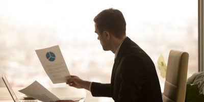 Business professional reviewing financial reports and compliance documents in an office environment.